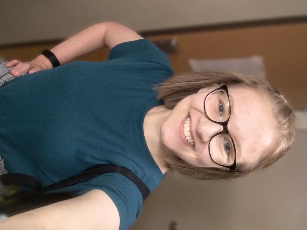 White woman with chin-length blonde hair wearing glasses and a teal tshirt