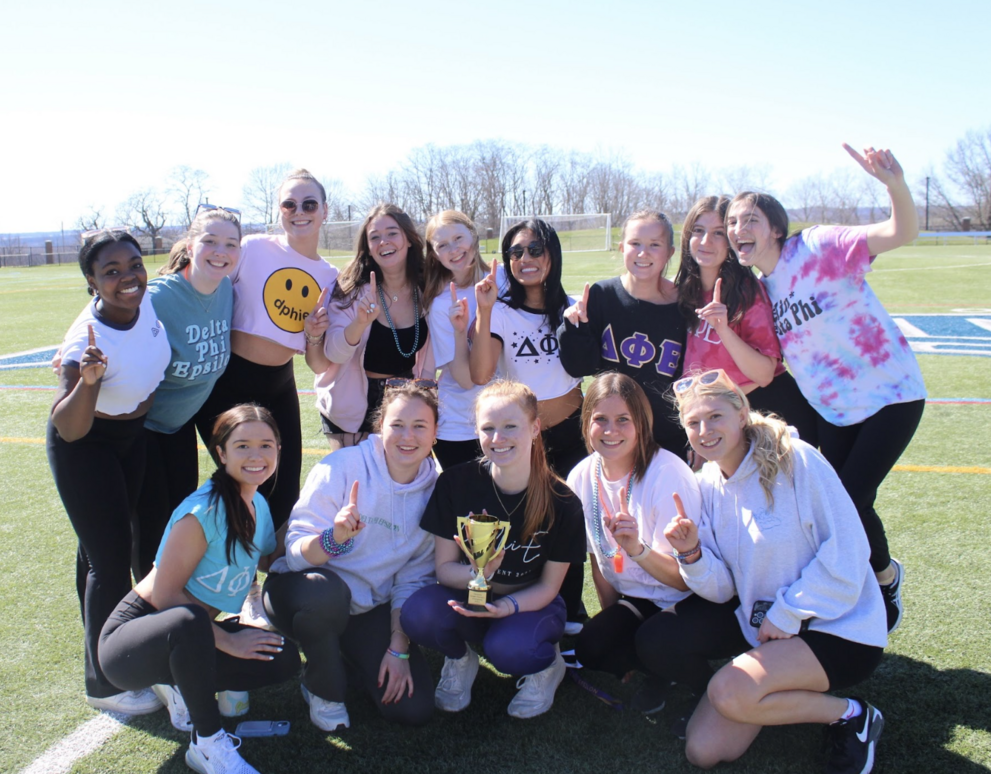 Group of students outside on a field smiling and holding a small trophy.