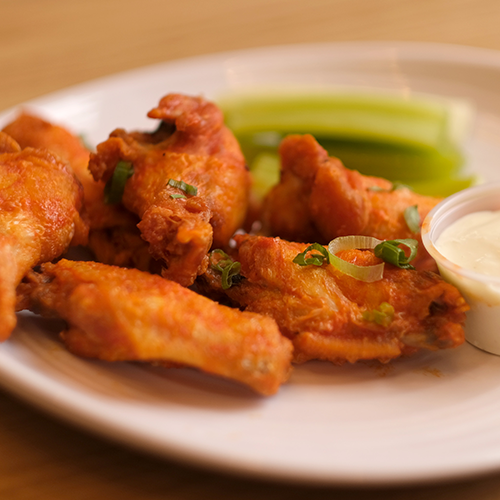 Buffalo chicken wings with celery sticks and a side of blue cheese.